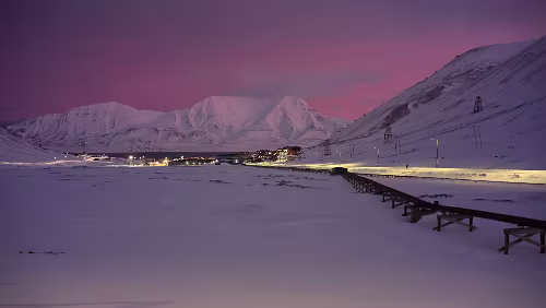 Rundgang Longyearbyen Blick vom „Vei 106“ auf Longyearbyen, links wo die schwarzen Schotterstreifen zu sehen sind, fließt im Sommer der „Longyearelva“. Rechts die oberirdischen Rohre...