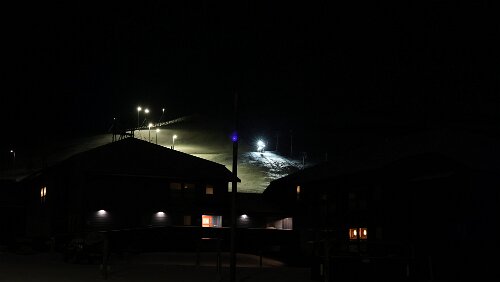 Longyearbyen Auf der Skipiste fährt ein Bagger ganz langsam herab, es sieht aus als ob er jeden Moment nach vorne kippen würde.