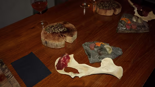 Huset Die Kostprobe. Auf dem oberen Holzstück (aus einem alten Telegrafenmasten gefertigt) ein Cräcker. Auf dem Rentierknochen eine Scheibe Rentier-Schinken, von...