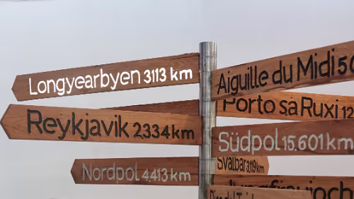 Wegweiser aus Stahlrohr mit Schildern aus Holz … und der ganze Pfosten wird von unten angestrahlt.